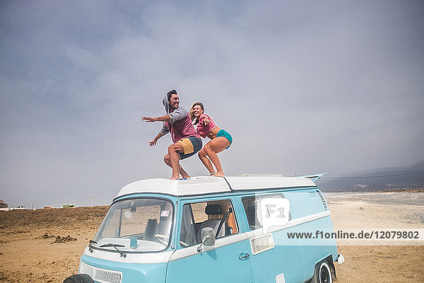 Spanien  Teneriffa  lachendes junges Paar steht auf dem Autodach und genießt Freiheit