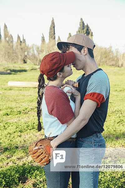 Junges Paar mit Baseballausrüstung beim Küssen im Park