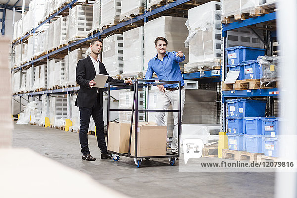 Businessmen in warehouse loading cardboard boxes on transport cart