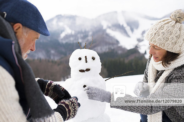 Senior couple building up snowman in winter landscape