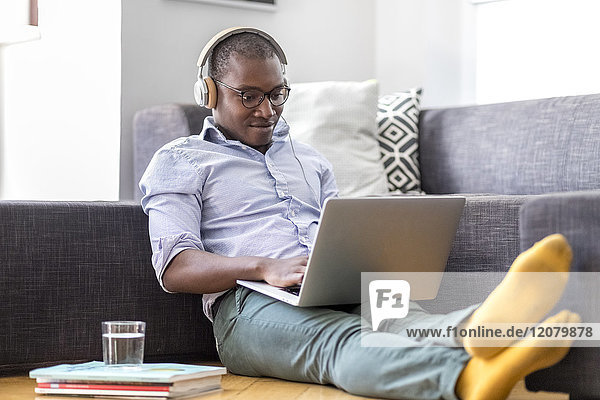 Young man sitting on the floor in the living room using laptop and headphones
