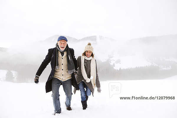 Porträt eines glücklichen Seniorenpaares beim Wandern in verschneiter Landschaft