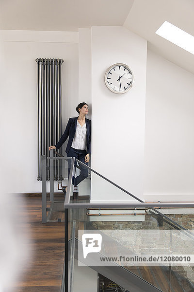 Businesswoman leaning against wall in office  waiting under clock