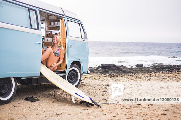 Laughing young woman with surfboard in van on the beach