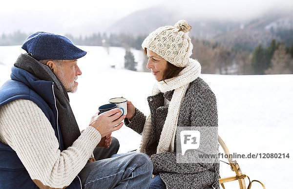 Seniorenpaar bei einer Pause mit heißen Getränken in verschneiter Winterlandschaft