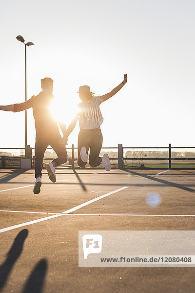 Unbeschwertes junges Paar springt bei Sonnenuntergang auf Parkebene