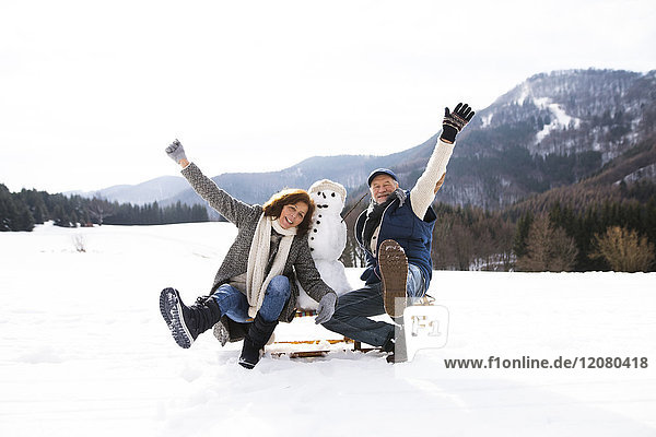 Senior couple posing with snowman on sledge in winter landscape