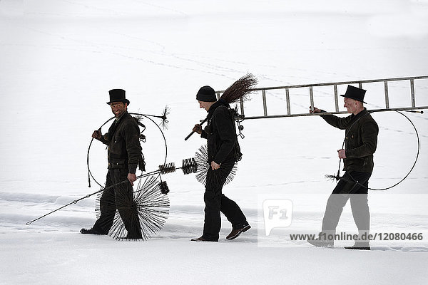Drei Schornsteinfeger im Schnee unterwegs