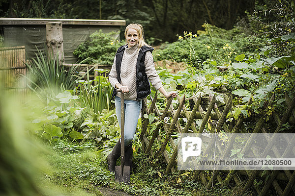 Porträt der lächelnden jungen Frau mit Spaten im Garten