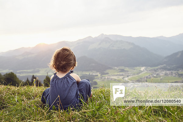 Austria  Tyrol  back view of little girl sitting on Alpine meadow looking at view