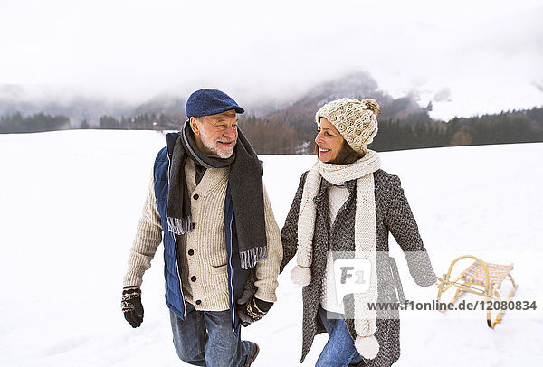 Glückliches Seniorenpaar mit Schlittenwanderung in verschneiter Landschaft