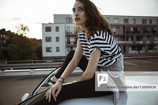 Seriöse junge Frau auf dem Autodach sitzend