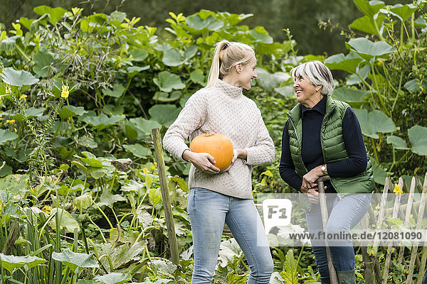 Happy young woman with her grandmother holding pumpkin in garden