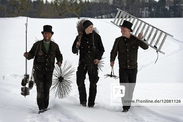 Three laughing chimney sweeps walking in snow