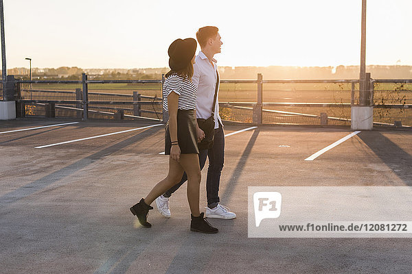 Junges Paar geht Hand in Hand auf Parkdeck bei Sonnenuntergang