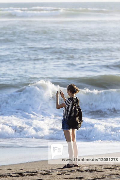 Indonesien  Bali  junge Frau beim Handyfoto am Strand