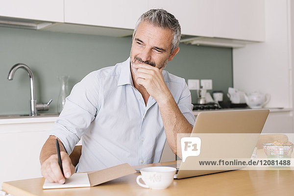 Lächelnder Mann beim Schreiben im Notebook und Laptop im Home-Office
