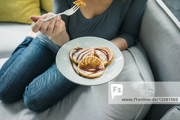 Nahaufnahme einer Frau, die auf der Couch sitzt und Pfannkuchen isst.
