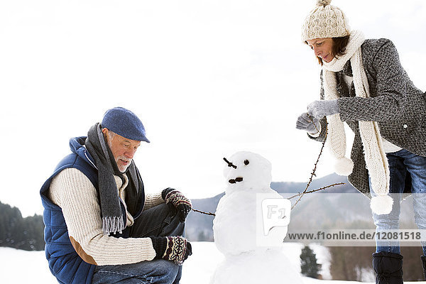 Senior couple building up snowman in winter