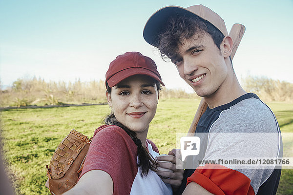 Porträt eines lächelnden jungen Paares mit Baseballausrüstung im Park