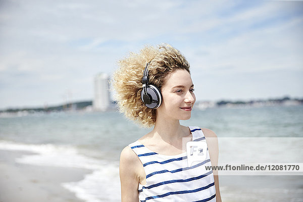 Portrait einer jungen blonden Frau mit Kopfhörer am Strand