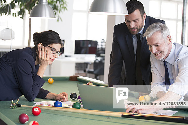 Business people standing at pool table with laptop  discussing investment strategy