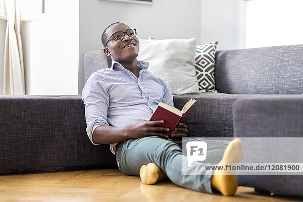 Happy young man sitting on the floor in the living room reading book