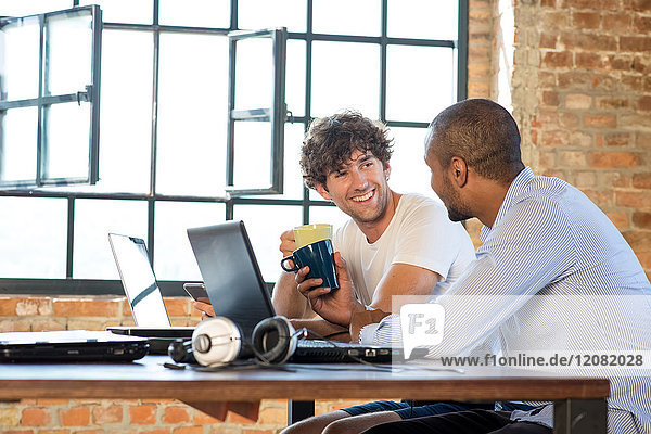 Two young businessmen working together in co-working space  using laptops