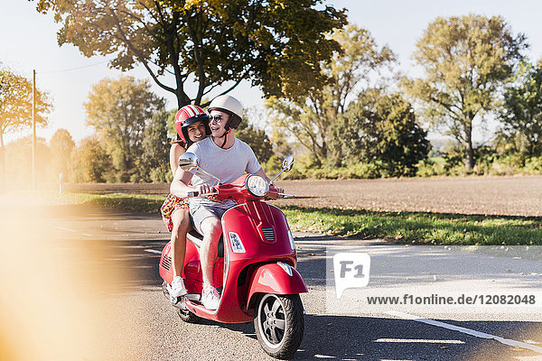Happy young couple riding motor scooter on country road