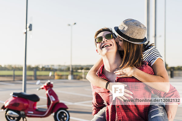 Happy young couple hugging on parking level with motor scooter in background