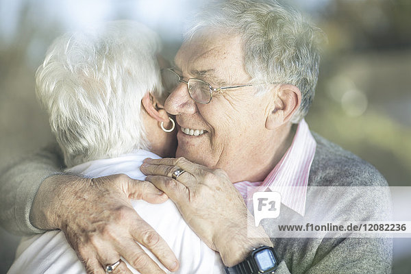 Fröhliches Seniorenpaar umarmt sich hinter der Fensterscheibe