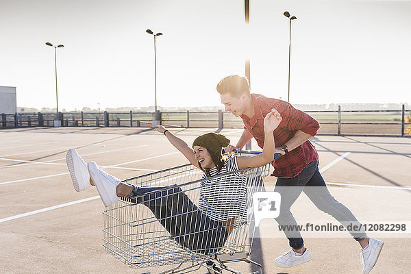 Playful young couple with shopping cart on parking level