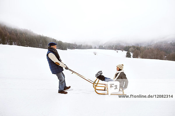 Senior couple having fun with sledge in snow-covered landscape