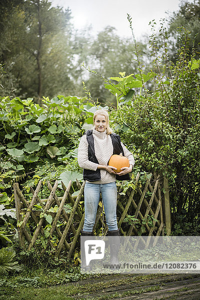 Portrait of smiling young woman holding pumpkin in garden