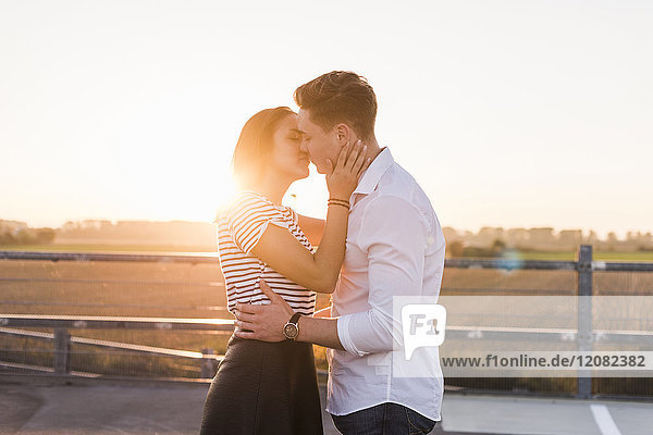 Young couple kissing on parking level at sunset