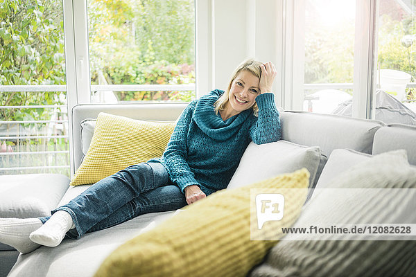 Porträt einer glücklichen Frau,  die sich auf der Couch entspannt.