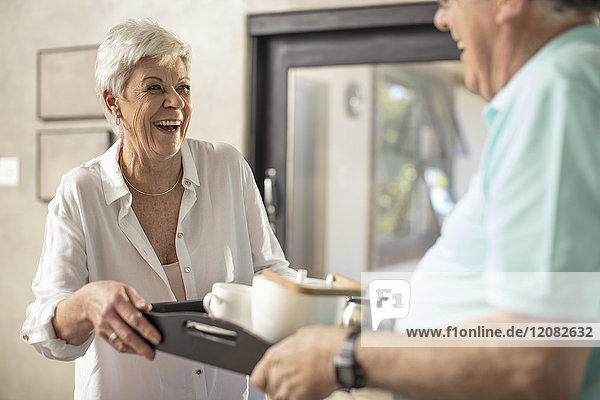 Glückliche Seniorin  die dem Ehemann Kaffee auf einem Tablett serviert.