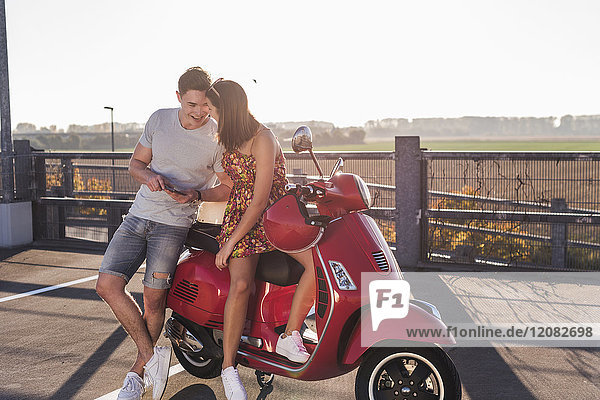 Happy young couple on parking level with motor scooter and cell phone