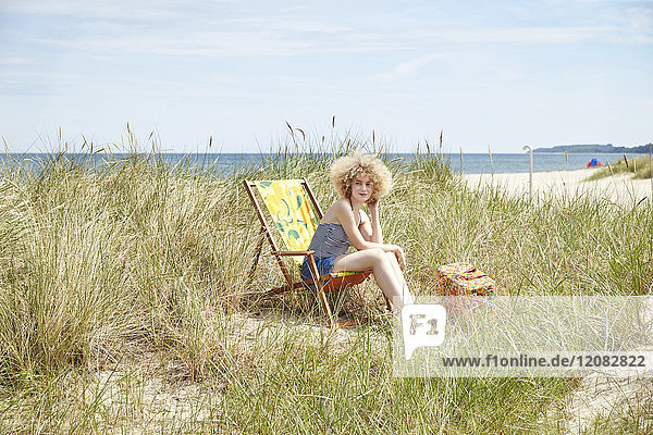 Junge Frau sitzt auf einem Strandkorb in den Dünen und beobachtet etwas.