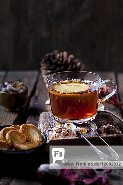 Glas schwarzer Tee mit Zitronenscheibe und Steinzucker auf Holztisch