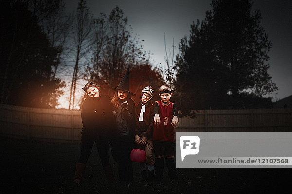 Portrait of boy and girls posed in halloween costumes in garden at dusk
