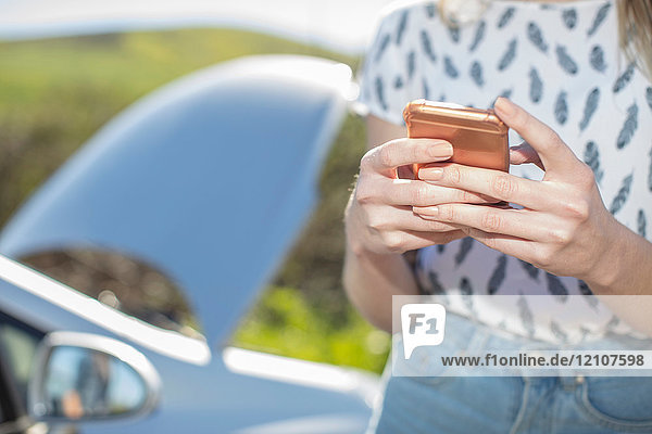 Junge Frau neben einem liegengebliebenen Auto  mit Smartphone  Mittelteil