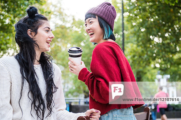 Two young stylish women laughing in city park
