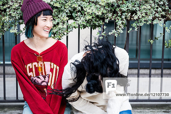Two young stylish women laughing on city bench