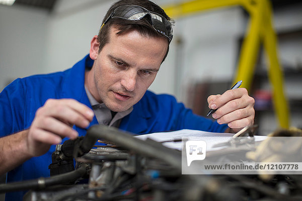 Male car mechanic with clip board checking car engine in repair garage