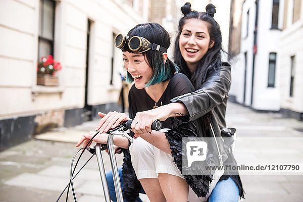 Zwei junge stilvolle Frauen radeln mit einem Retro-Fahrrad die Straße entlang