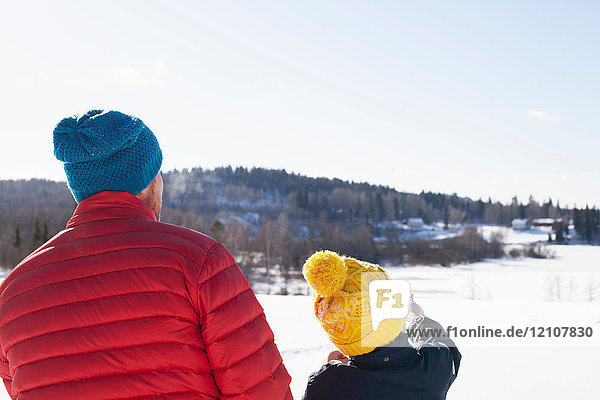 Rear view of man and son looking out and pointing over snow covered landscape