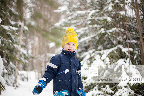 Portrait of boy in yellow knit hat walking in snow covered forest