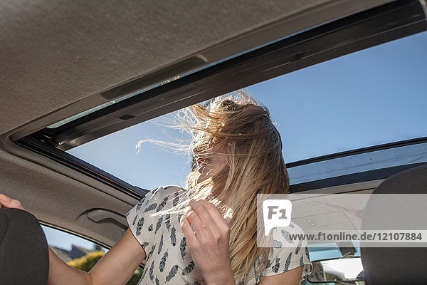 Junge Frau im Auto  die aus dem offenen Schiebedach schaut