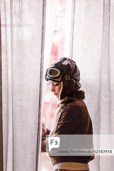 Girl looking out through window wearing pilot costume for halloween
